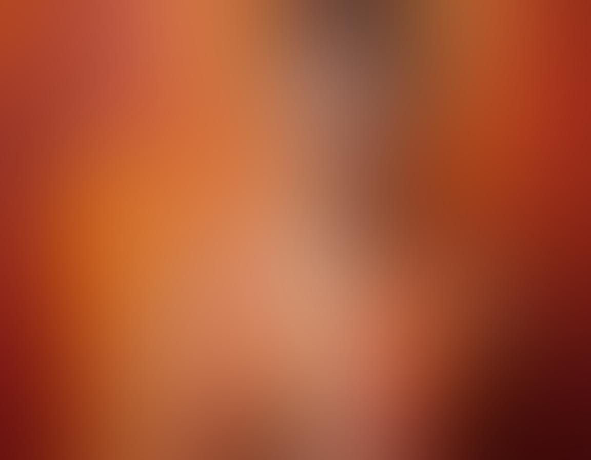 A stunning adult photography scene that captures the essence of skin as a canvas, featuring an elegant model artfully positioned in a dramatic pose, surrounded by paint splashes and artistic textures. The background showcases a soft gradient of warm colors, with light playing across the skin to highlight form and contours. The mood of the image is both intimate and empowering, blending the elements of visual narrative and artistry. super-realistic. vibrant colors. soft focus.